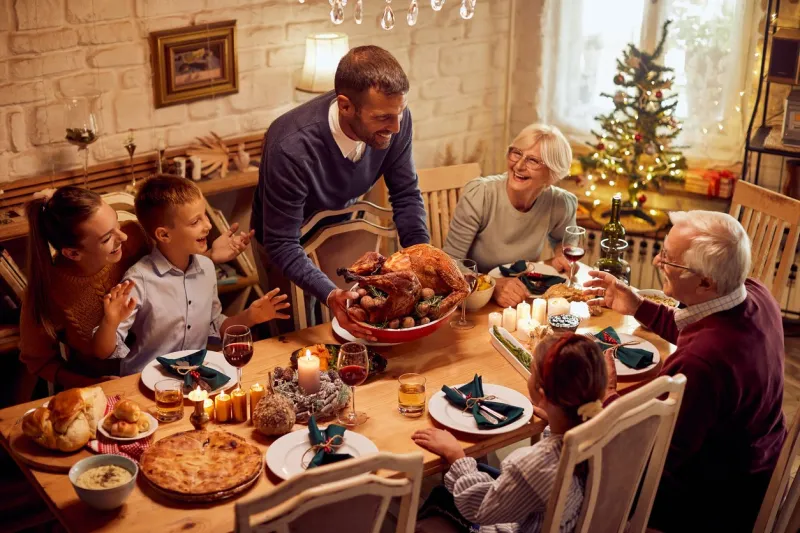 happy extended family celebrating thanksgiving and having traditional meal at dining table focus is on man serving roast turkey