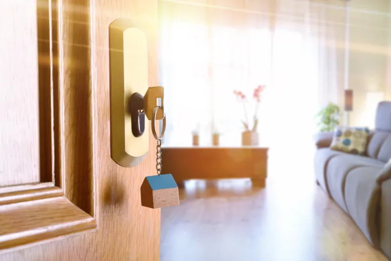open entrance door detail of a house with keys in the lock and furnished living room in the background with golden light effect
