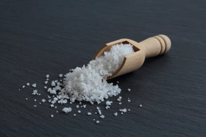 crystals of natural higth quality sea salt from guerande - france harvested by hand and named fleur de sel in a wooden spoon on the slate surface
