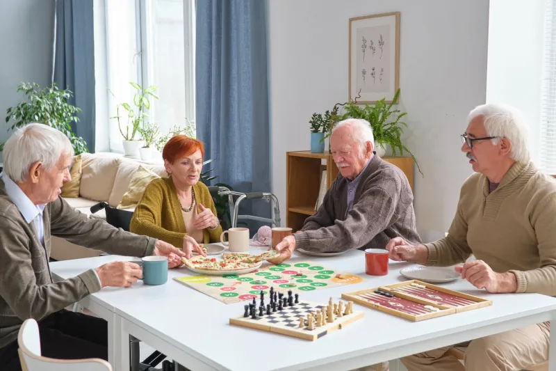 group of elderly friends eating pizza at the table after board game in the living room