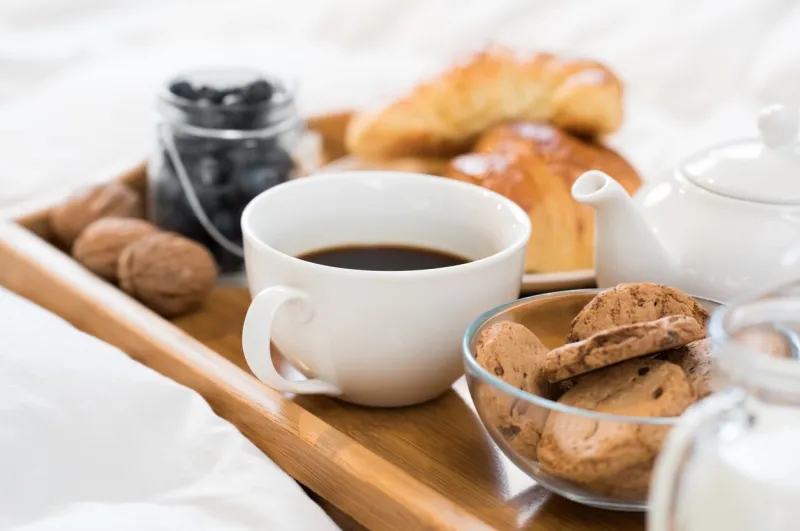 breakfast in bed with hot coffee and croissants healthy breakfast kept on bed close up of a cup of tea with cookies on wooden tray in bed