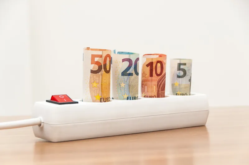 euro banknotes inserted into an extension socket on a wooden surface expensive concepts of energy and cost of electricity front view