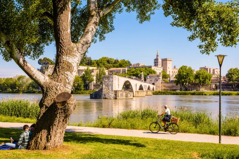 avignon, france - may 16, 2018  people are biking or resting by a sunny day on the banks of the rhone, opposite the saint-benezet bridge, also known as avignon bridge, and the papal palace