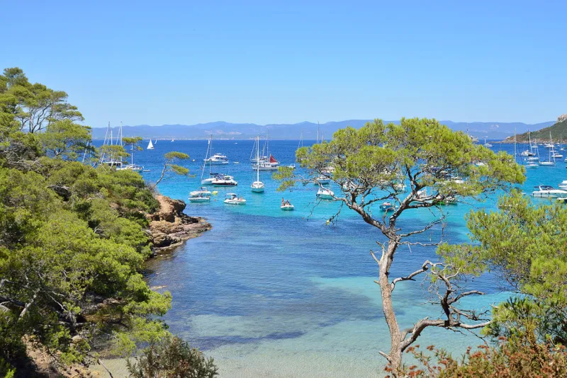 view of beach with boats in clear sea in the island of porquellores in the french riviera in france