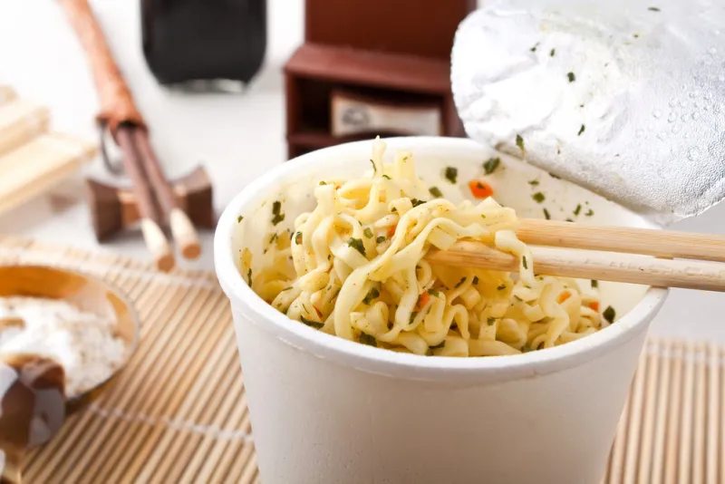 cup of ramen noodles raised on chopsticks