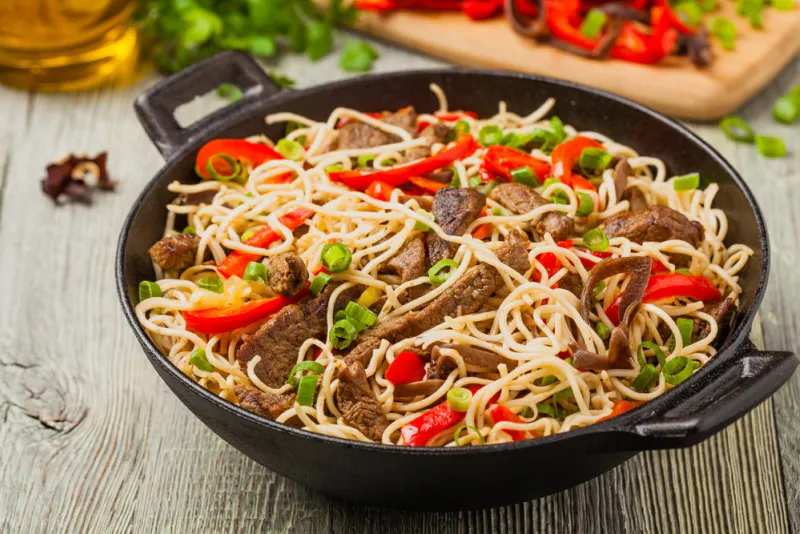 chinese pasta with beef prepared in wok wooden background front view