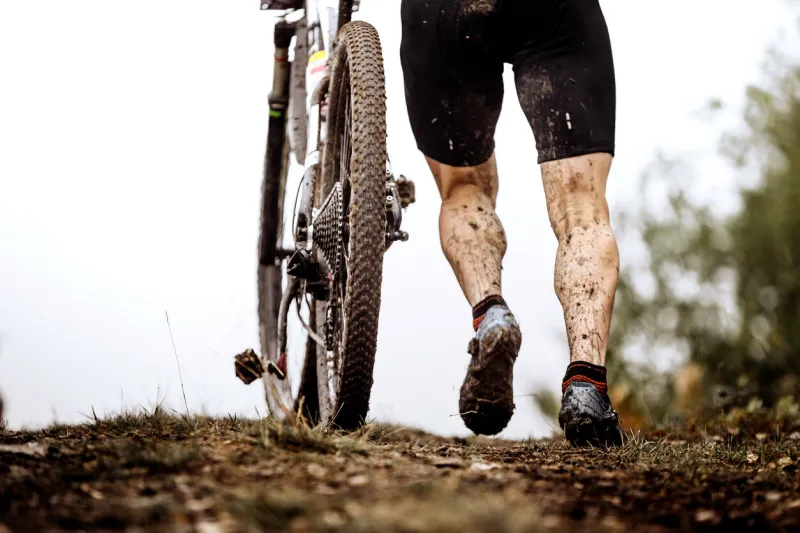 back athlete cyclist with dirty mountain bike climb uphill