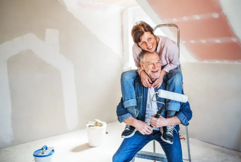 portrait of cheerful senior couple painting walls in new home, having fun relocation concept