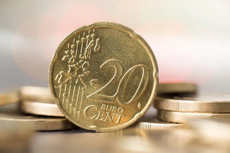 closeup of a 20 euro cent coin standing between other coins with a smooth blur in the foreground and the background