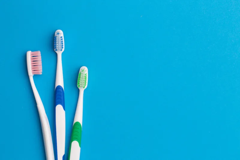 three colorful toothbrushes empty blue background, place for inscription
