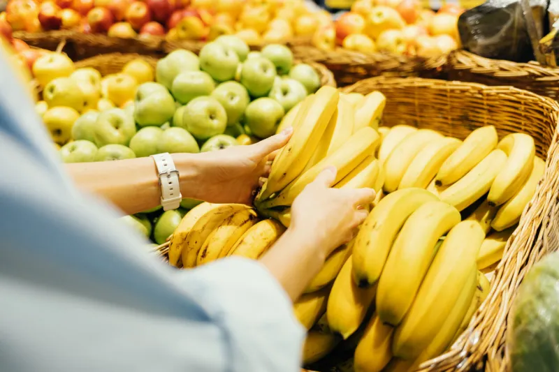 shopping for groceries, close-up female hands take fresh bananas from store shelf