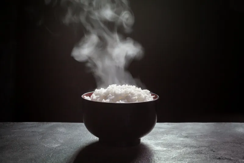 cooked rice with steam in black bowl on dark background,hot cooked rice in bowl selective focus,hot food and healthy
