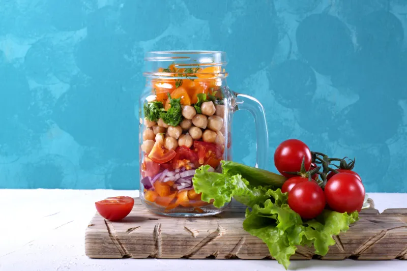 layered salad with chick peas and vegetables in mason jar against the blue wall