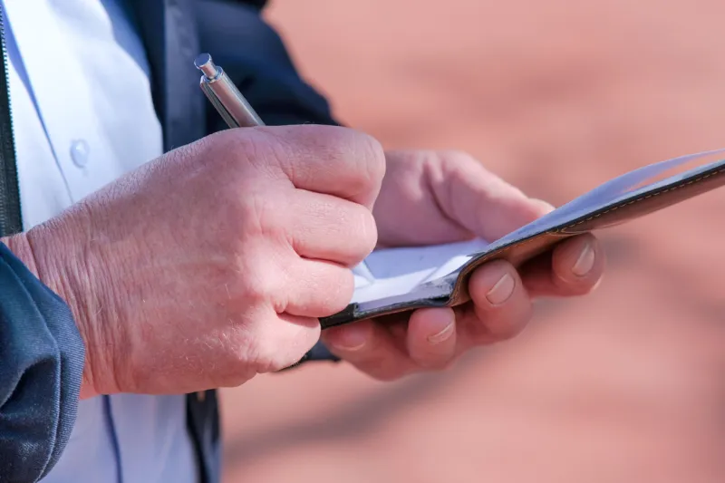 close-up side view of a police officer or employee of the public regulatory office taking notes in his pad - selective focus, a lot of depth of field, copy space