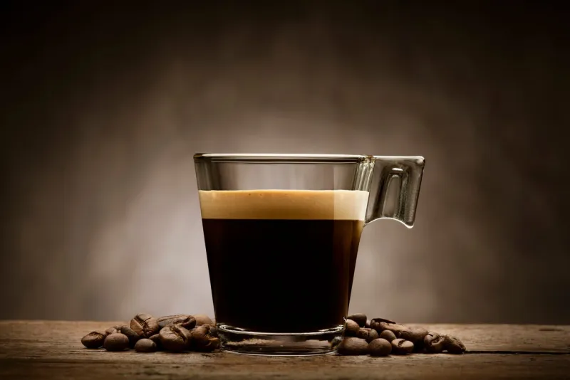 black coffee in glass cup with coffee beans on wooden table