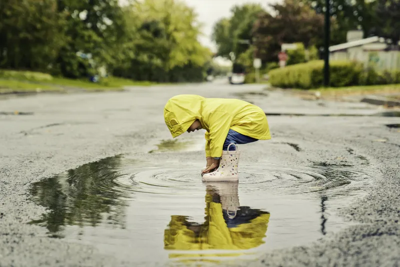 a funny cute baby girl wearing yellow waterproof coat and boots playing in the rain