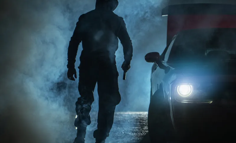 hooded gang member with a handgun walking away next to his car shooting aftermath concept short-barrelled firearm