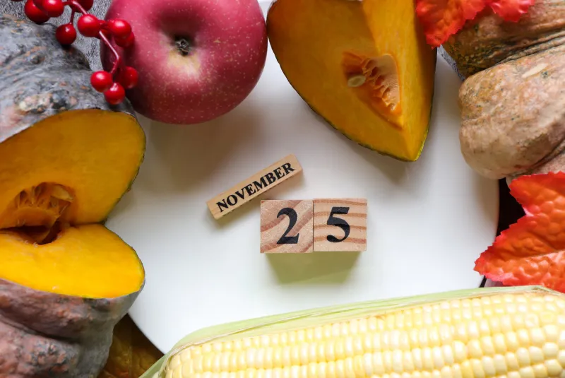 november 25th, cube wooden calendar showing date on 25 november, table decorated with pumpkins ,corn and applethanksgiving celebration traditional concept