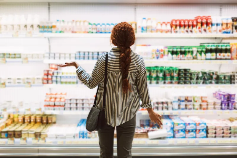 young woman in striped shirt from back trying choose dairy products in modern supermarket