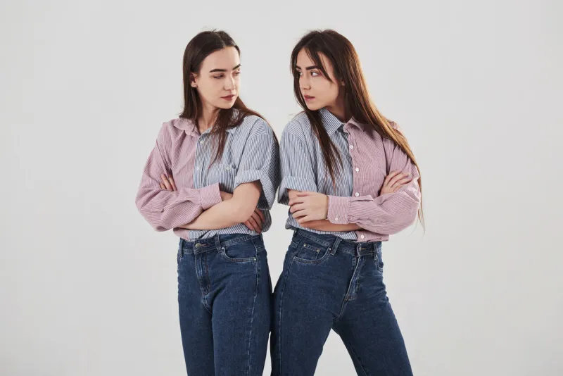 offended and look at other with anger two sisters twins standing and posing in the studio with white background