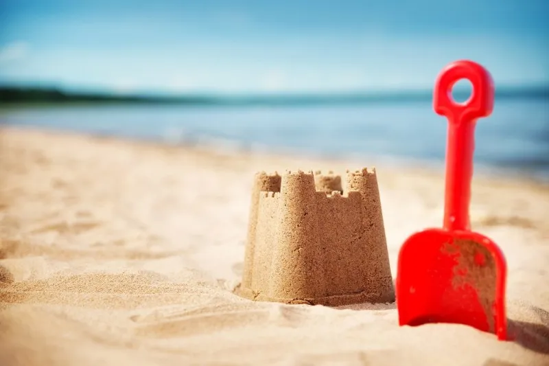 sandcastle with a shovel on the sea in summertime seashore on beautiful day sand on the beach and blue water