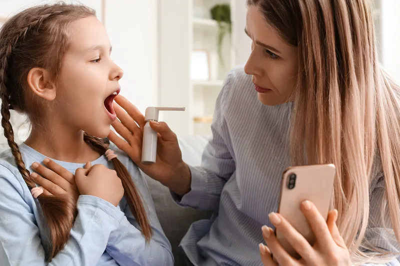 little girl suffering from sore throat and her mother video chatting with doctor at home