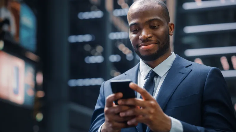 portrait of successful african-american businessman on the street of the central business district in big city black digital entrepreneur uses mobile phone e-commerce app for stock market investment