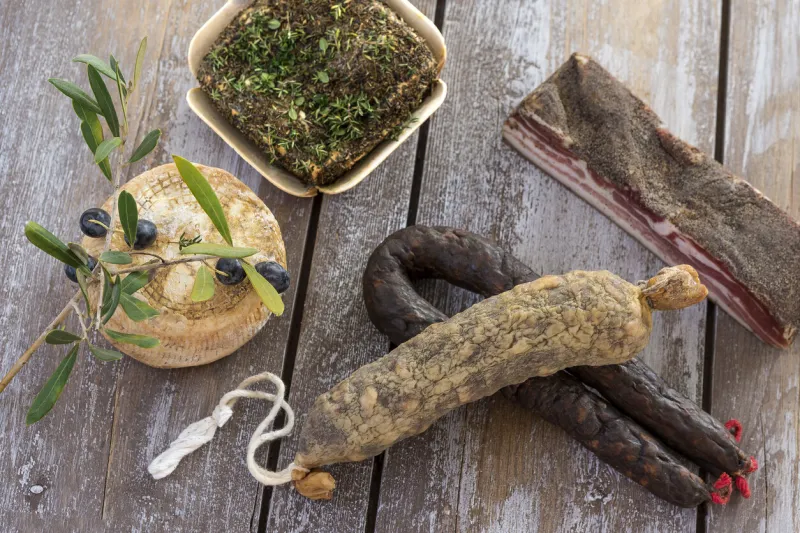 several variety of traditional corsican charcuterie on a wooden background with an olive branch and black olives
