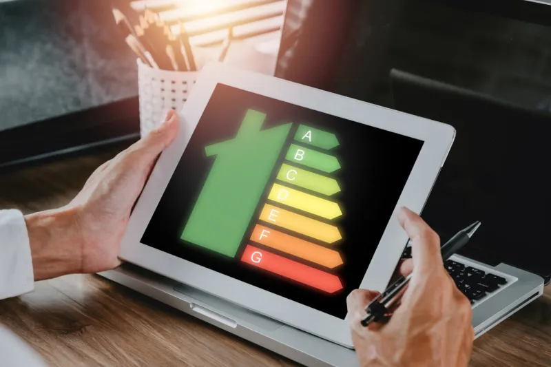 person hand using digital tablet with house icon energy efficiency scale image on office desk, concept of ecological and bio energetic house energy class