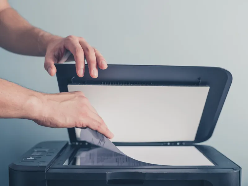 the hands of a young man is placing a piece of paper on a flatbed scanner in preparation for copying it