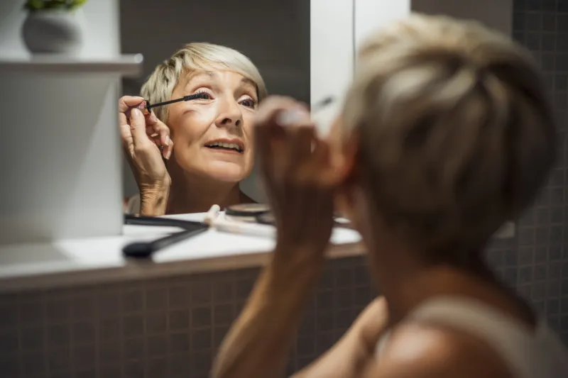mature woman is applying mascara in the bathroom