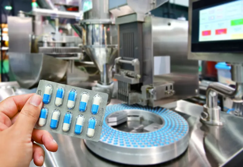 hand holding blue capsule pack at medicine pill production line, industrial pharmaceutical concept