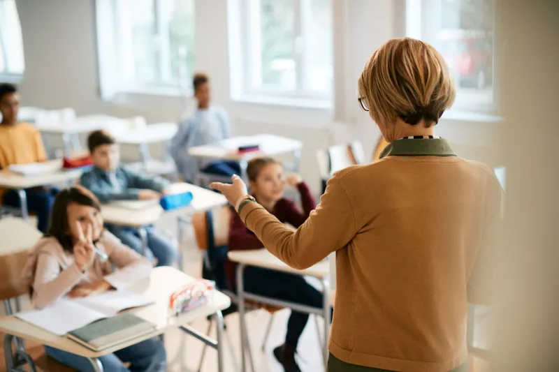 rear view of elementary school teacher pointing at one of her students who is raising arm to answer a question