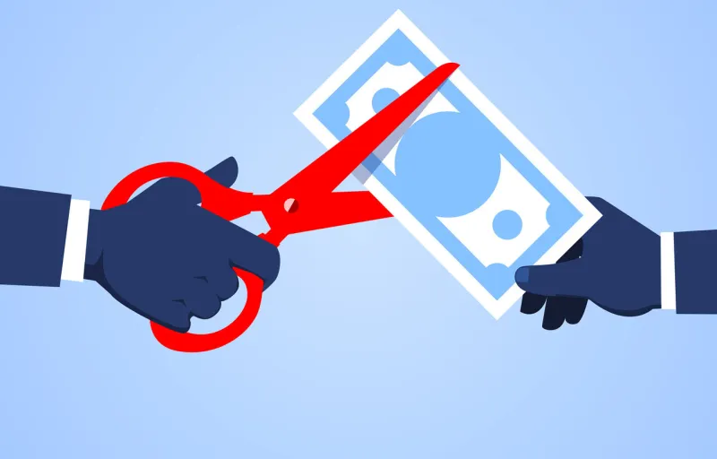 hand holding scissors to cut banknotes