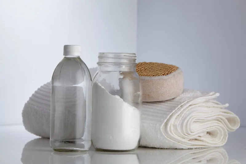 white vinegar and baking soda with scrub sponge and white towel
