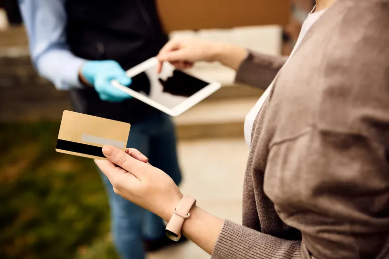 close-up of woman receiving package from deliverer and paying with her credit card