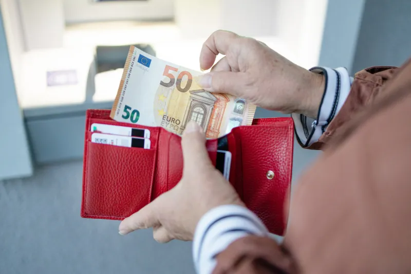 unrecognizable female holding in hands wallet with euro money near the atm withdrawing cash to pay for services, a loan or study