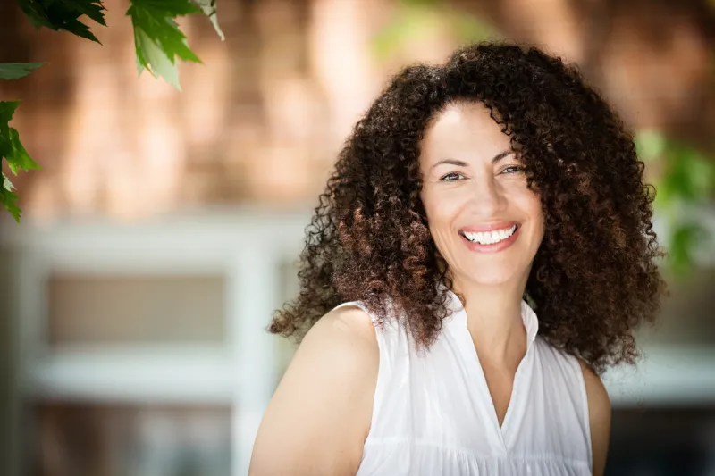 mature ethnic woman smiling at the camera she is outside in front of her house