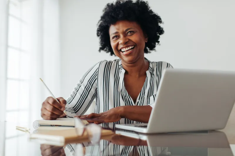 portrait of a smiling woman sitting at table with laptop and dairy woman smiling at camera while working from home office