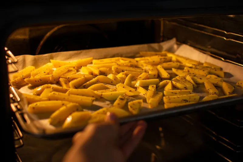 hand putting tray with cut potatoes into the oven to make a healthy homemade french fries vegan and vegetarian fast food and cooking