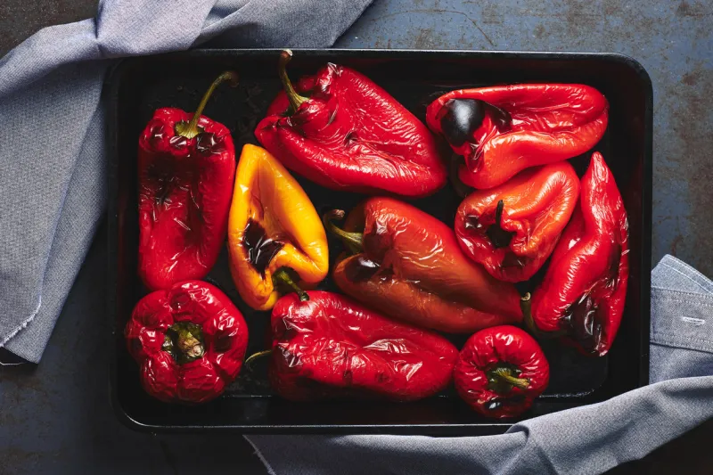 roasted red and yellow peppers in baking tray on a dark background top view