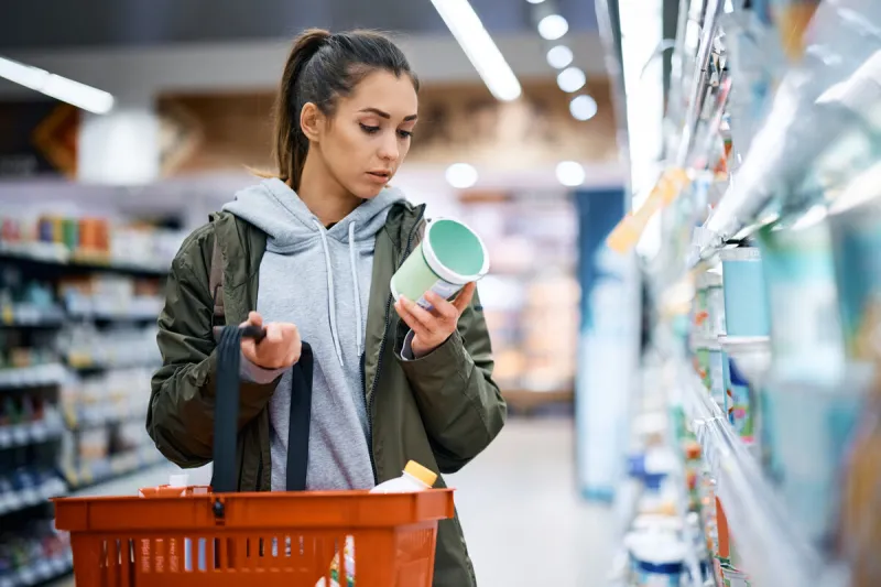 young woman reading nutrition label while buying diary product in supermarket
