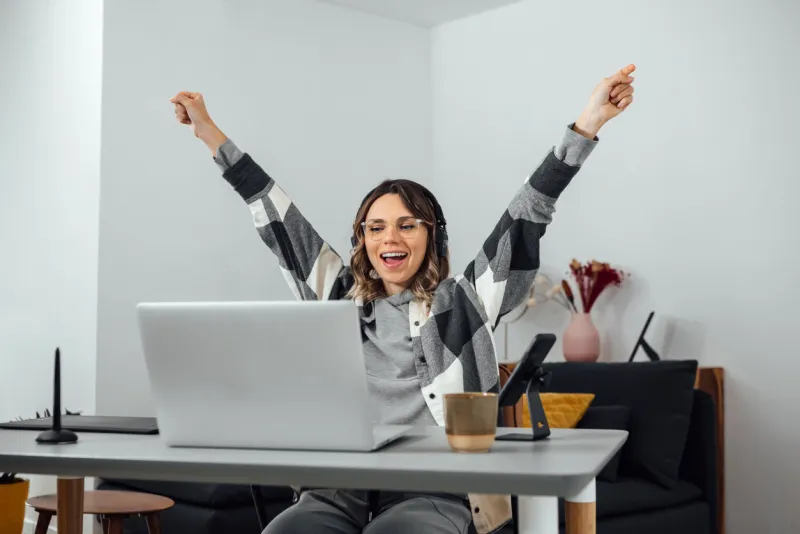 excited woman, with arms opened, sitting at home office businesswoman freelancer celebrating success with raised hands overjoyed, euphoric, receiving good news at laptop, triumph, win lottery