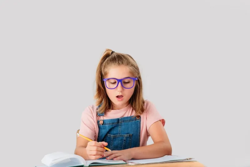 a nine year old student is working at her school desk wearing jeans overall and glasses she is looking for an answer or something to write she is in a studio she is in quebec, canada