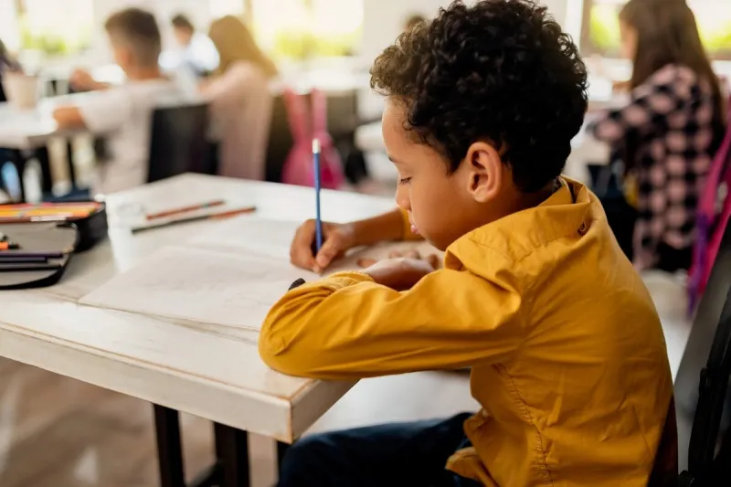 black elementary student writing on the paper while having exam in the classroom