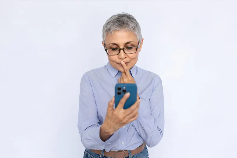 portrait of pensive senior woman reading message on mobile phone mature caucasian woman wearing eyeglasses and blue shirt touching lip while reading newsletter mobile communication concept