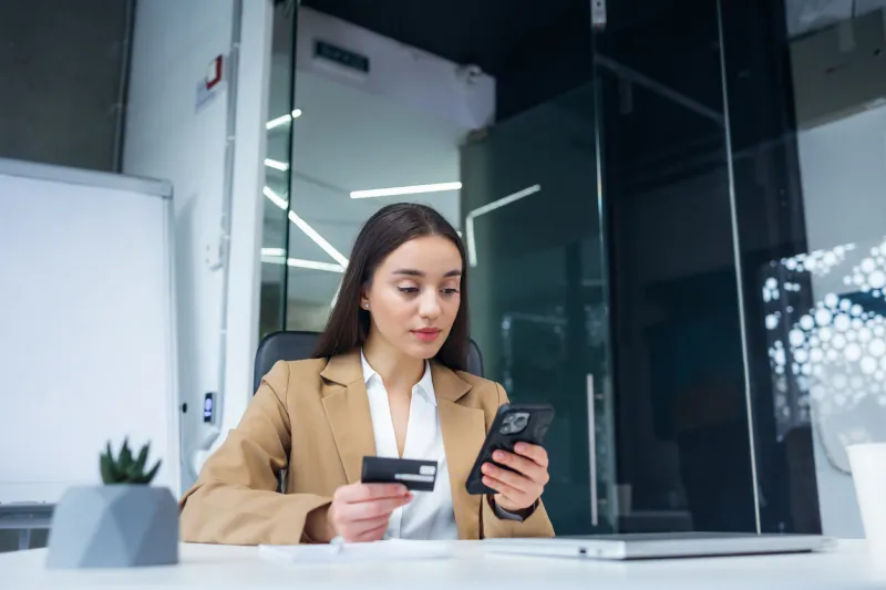 caucasian woman using smartphone shopping online holding credit card making payment sitting at desk at office internet banking application and e-commerce