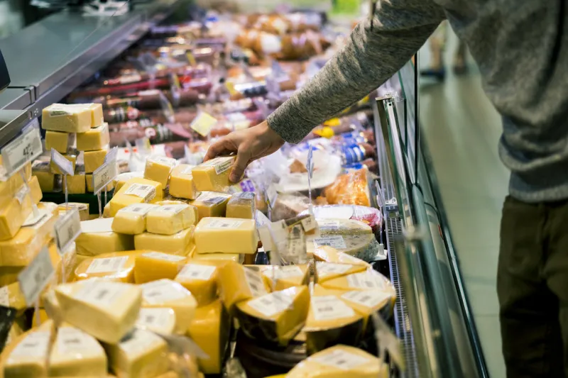 close up person choosing piece of cheese in food shop