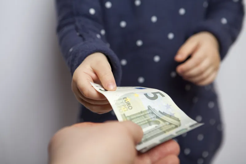 small child hand takes five euros banknote from adult hand