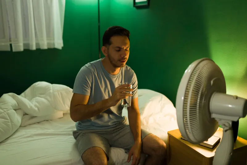 attractive young man feeling thirsty and hot in the middle of the night hispanic man turning on the fan in his bedroom